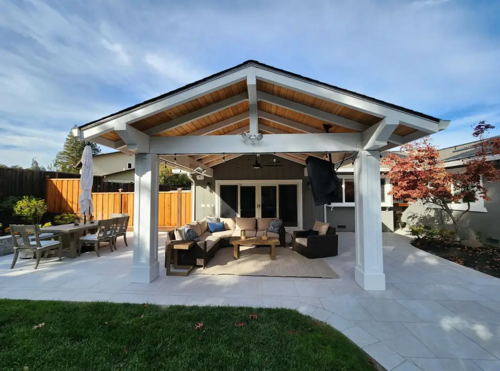Solid roof pavilion with white beams and a cedar ceiling over an outdoor sectional, with a dining table and a Japanese maple on a porcelain tile patio