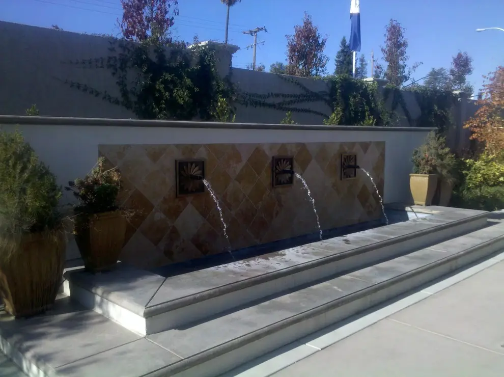 Wall fountain with three spouts over a diamond pattern stone tile backdrop and a two-step ledge, flanked by potted plants, in Mountain View