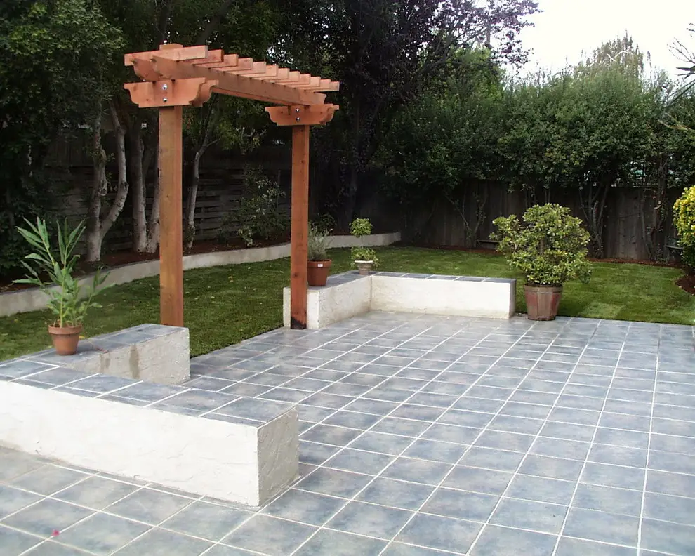 Tile patio with stucco seat walls and a small wood pergola entry frame, beside a lawn with potted plants